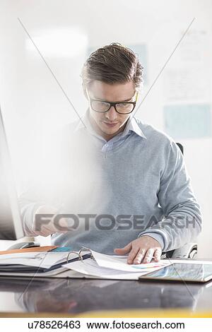 Stock Image - Young businessman busy with paperwork at office desk. Fotosearch