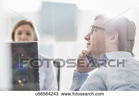 Stock Image - Young businessman chatting on smartphone at office desk. Fotosearch