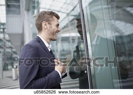 Stock Photograph - Young businessman checking his reflection in office window. Fotosearch