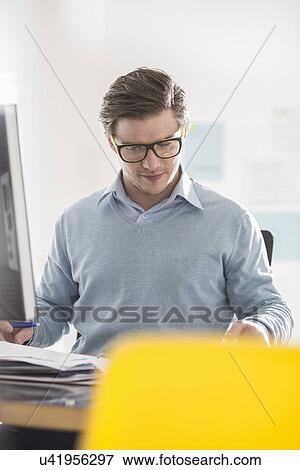 Young businessman doing paperwork at office desk View Large Photo Image Stock Photo - Young businessman doing paperwork at office desk. Fotosearch