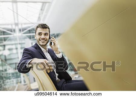 Young businessman in airport departure lounge chatting on smartphone View Large Photo Image Picture - Young businessman in airport departure lounge chatting on smartphone. Fotosearch