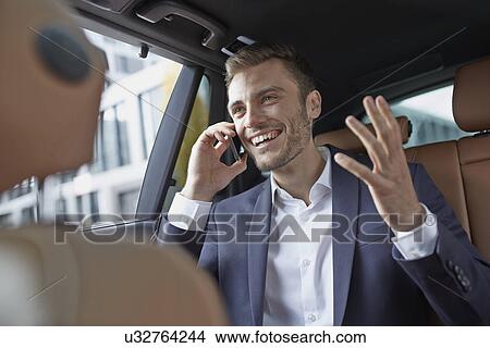 Young businessman in taxi back seat chatting on smartphone View Large Photo Image Picture - Young businessman in taxi back seat chatting on smartphone. Fotosearch