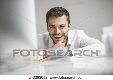 Young businessman laughing at office desk View Large Photo Image Stock Photo - Young businessman laughing at office desk. Fotosearch