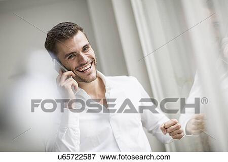 Young businessman laughing whilst chatting on smartphone in office View Large Photo Image Stock Photo - Young businessman laughing whilst chatting on smartphone in office. Fotosearch