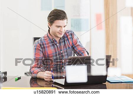 Young businessman looking at laptop on office desk View Large Photo Image Stock Image - Young businessman looking at laptop on office desk. Fotosearch