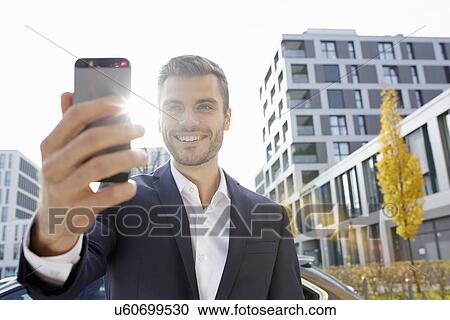 Stock Image - Young businessman on street reading smartphone text. Fotosearch