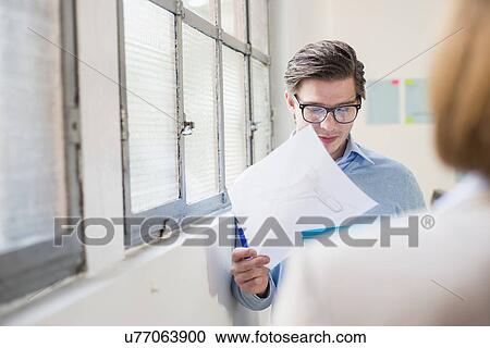Stock Image - Young businessman reading paperwork in office. Fotosearch