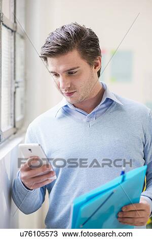 Stock Image - Young businessman reading texts on smartphone in office. Fotosearch