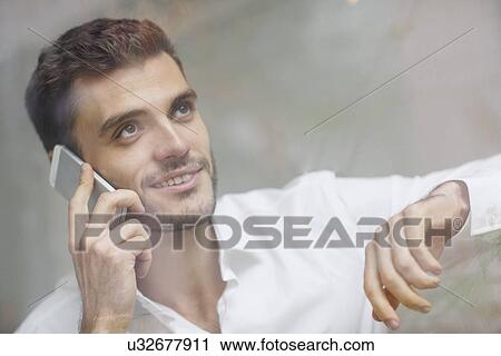 Young businessman resting on elbow whilst chatting on smartphone View Large Photo Image Stock Image - Young businessman resting on elbow whilst chatting on smartphone. Fotosearch