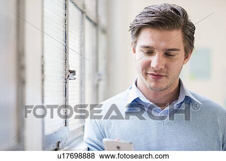 Stock Photo - Young businessman texting on smartphone in office. Fotosearch