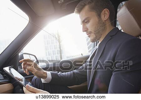 Stock Photography - Young businessman using touchscreen on digital tablet in car. Fotosearch
