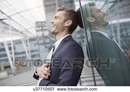 Stock Photo - Young businessman with digital tablet leaning against office window. Fotosearch