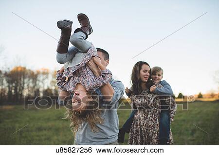 Young couple carrying son and daughter in field View Large Photo Image Stock Photograph - Young couple carrying son and daughter in field. Fotosearch