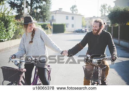Stock Photo - "Young couple cycling, holding hands". Fotosearch