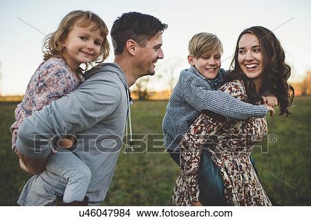 Young couple giving son and daughter piggy backs in field View Large Photo Image Picture - Young couple giving son and daughter piggy backs in field. Fotosearch