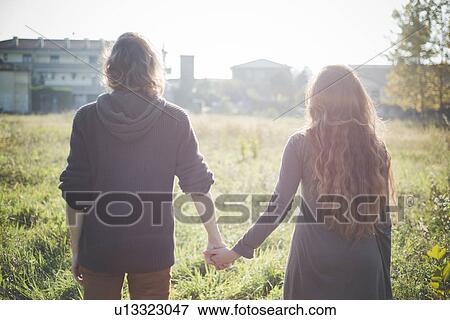 Young couple holding hands in field in sunlight View Large Photo Image Stock Photo - Young couple holding hands in field in sunlight. Fotosearch