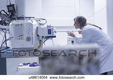 Picture - Young female scientist in lab using scanning electron microscope. Fotosearch