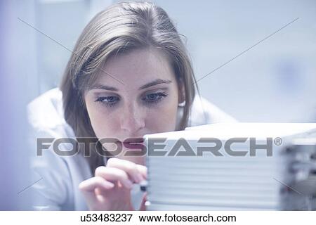 Stock Photo - Young female scientist in lab using control panel on scanning electron microscope. Fotosearch