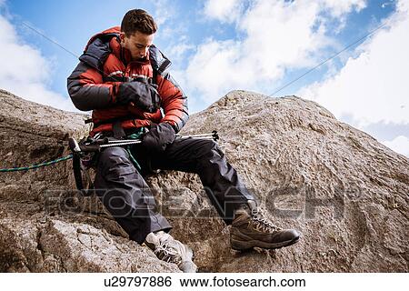 Stock Photograph - "Young male climber on rock checking rope, The Lake District, Cumbria, UK". Fotosearch