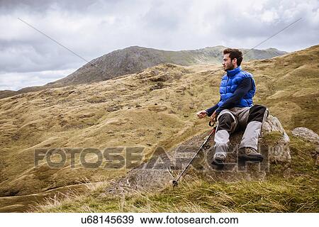 Stock Photo - "Young male hiker looking out over landscape, The Lake District, Cumbria, UK". Fotosearch