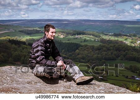 Picture - "Young male hiker opening flask on top of Guise Cliff, Pateley Bridge, Nidderdale, Yorkshire Dales". Fotosearch