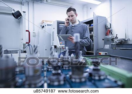 Young male technician ordering on smartphone whilst using digital tablet in workshop View Large Photo Image Stock Photo - Young male technician ordering on smartphone whilst using digital tablet in workshop. Fotosearch