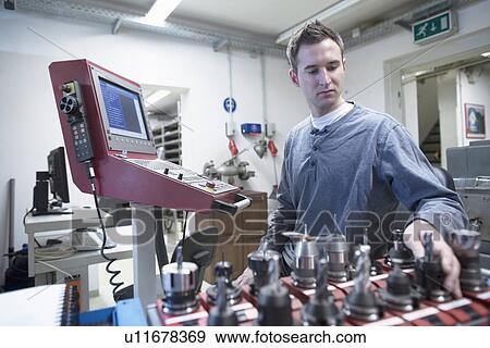 Stock Photo - Young male technician picking drill bit in workshop. Fotosearch
