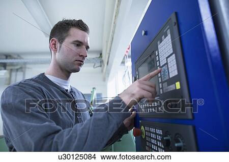 Picture - Young male technician using control panel for equipment in workshop. Fotosearch