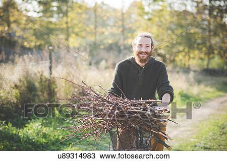 Stock Image - Young man carrying bunch of sticks on bicycle. Fotosearch