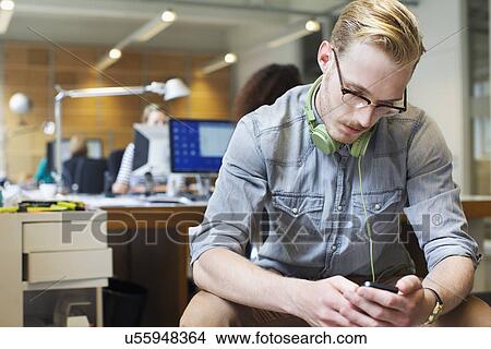 Picture - Young man choosing music from smartphone in office. Fotosearch