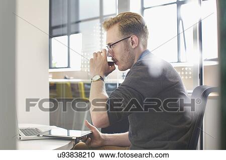 Young man drinking at office desk View Large Photo Image Stock Image - Young man drinking at office desk. Fotosearch