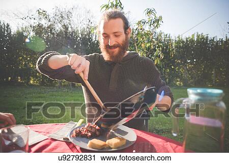 Stock Image - Young man holding frying pan serving food. Fotosearch