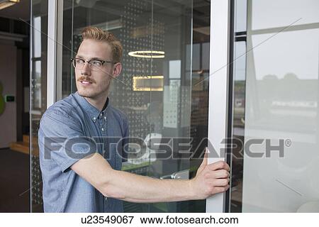 Stock Photo - Young man looking over his shoulder from office doorway. Fotosearch