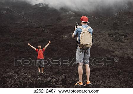 Stock Photo - "Young man photographing friend at Pacaya volcano, Antigua, Guatemala". Fotosearch