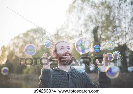 Picture - Young man playing with bubbles. Fotosearch