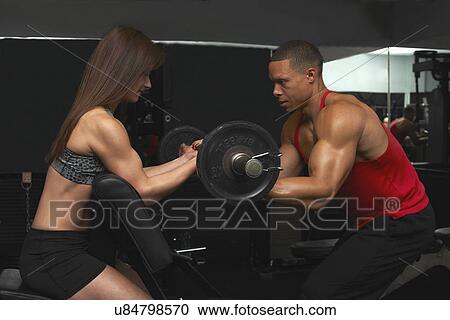 Stock Image - "Young woman and mid adult man, lifting weights". Fotosearch
