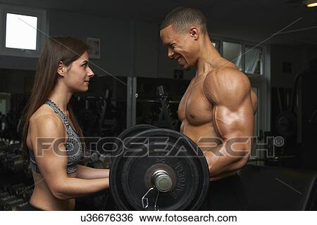 Stock Photograph - "Young woman and mid adult man, lifting weights". Fotosearch