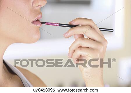 Stock Photography - "Young woman applying lipstick with lip brush, close-up". Fotosearch