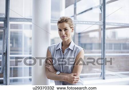 Stock Image - "Young woman crossing arms, leaning against pillar". Fotosearch