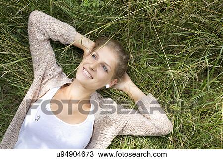 "Young woman laying in grass, hands behind head" View Large Photo Image Stock Image - "Young woman laying in grass, hands behind head". Fotosearch