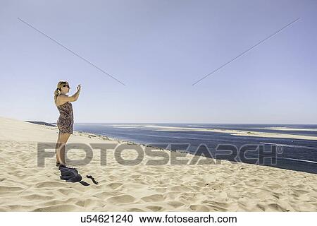"Young woman photographing sea with smartphone, Dune de Pilat, France" View Large Photo Image Stock Image - "Young woman photographing sea with smartphone, Dune de Pilat, France". Fotosearch