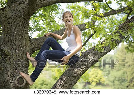 Stock Photography - Young woman sitting on tree branch. Fotosearch