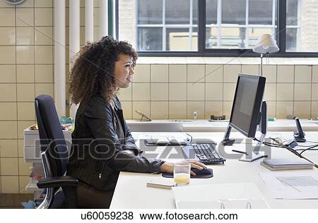 Stock Photo - Young woman using computer at office desk. Fotosearch