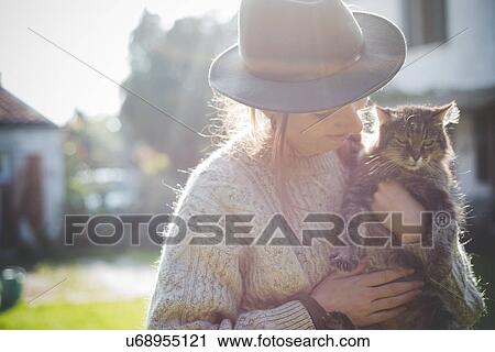 Stock Image - "Young woman wearing hat, holding cat". Fotosearch