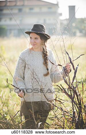 Young woman wearing hat touching plants in field View Large Photo Image Stock Photo - Young woman wearing hat touching plants in field. Fotosearch
