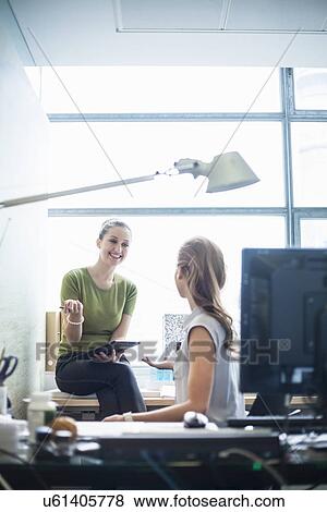 Stock Photo - Young women chatting in office. Fotosearch
