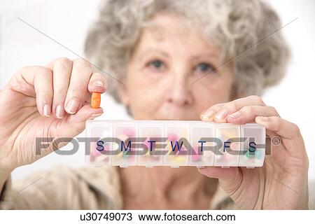 Stock Image - Woman holding pill and pill container. Fotosearch