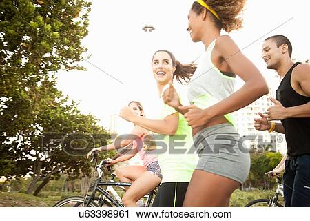 Adult friends running and cycling in park View Large Photo Image Stock Image - Adult friends running and cycling in park. Fotosearch