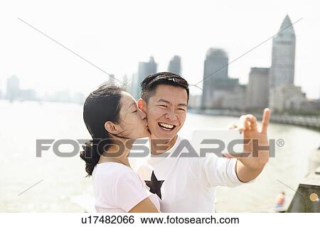 Stock Photograph - "Affectionate tourist couple taking smartphone selfie, The Bund, Shanghai, China". Fotosearch