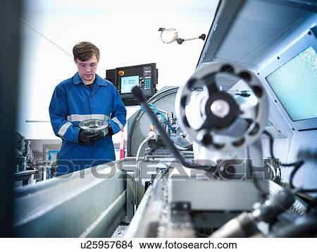 Apprentice engineer holding steel component with lathe in engineering factory View Large Photo Image Picture - Apprentice engineer holding steel component with lathe in engineering factory. Fotosearch